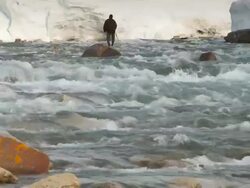 A man goes fishing in a freshwater stream for Arctic Char, massive snow banks enclose the river Stock Footage