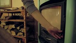 Woman putting wood on a wood burning stove Stock Footage