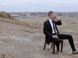 MS Young businessman dressed in  black suit  sitting on  chair and talking on cell phone on top of  bluff in  rural area / Maple Grove, Minnesota, United States Stock Footage