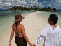WS young man and woman holding hands walking along idyllic sandbar towards tropical island in background / Snake Island, Bacuit Archipelago, El Nido, Palawan, Philippines Stock Footage