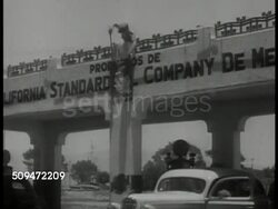 1935: MEXICO OIL PROPERTY: WS 'Pierce' Oil trucks leaving parking lot. LA WS Mexican man hanging Lazaro Cardenas caricature poster on bridge overpass. MS Poster put on wall over 'Pennsylvania' sign. VS Poster over 'Pierce Co.', over gas station sign. Instructional Video