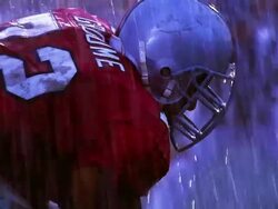 OVEREXPOSED MS football player snaps ball into play, opposing players tackle / rain Stock Footage