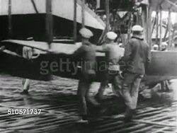 1917: US NAVY SEAPLANE: VS Sailors pushing hydroplane 'flying boat' out of hangar, turning boat on dock, pushing backward into water, sailors loading bomb, mounting machine gun, aircraft taxiing away on water.   WWI, aviation, possibly Curtiss. Instructional Video