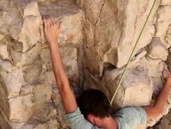 Handheld tilting shot of a rock climber making his way up a rectangular cliff. Stock Footage