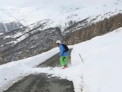 Skier descends across mountain road, jumps off of curb Stock Footage