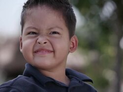Little Latino boy sitting in a wheelchair in front of a rock and flower garden Stock Footage