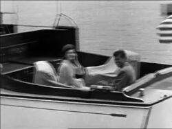 B/W 1961 PAN John + Jacqueline Kennedy riding on cabin cruiser pulling away / Hyannis Port Stock Footage
