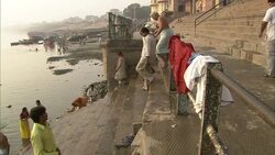 Two friends help a gray-haired man wrapped in a dhoti walk down the steps of a ghat. Stock Footage