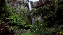 Man traverses highline stretched above waterfall, valley Stock Footage