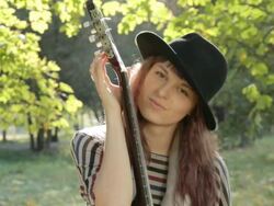 Young woman flirting, posing in park, holding guitar, smiling outdoors. Stock Footage