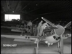 1945: ENGLAND AIRCRAFT FACTORY: INT MS Men pushing airplane engine on cart. VS Mechanics working on rows of fighter airplanes. MS Crane moving propellers into place. CU British woman working on airplane. Instructional Video