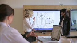 Female architects leading meeting discussing blueprints at monitor in conference room Stock Footage