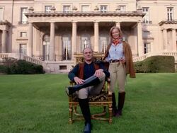 Wide shot portrait of wealthy couple in equestrian clothing in front of mansion (man sitting on chair) Stock Footage