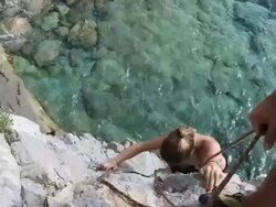 Detail of man belaying young woman on rock climb above sea Stock Footage