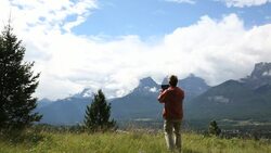 Middle aged man walks through mountain meadow and takes a picture with his tablet Stock Footage