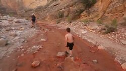 Young hiker boy skips through river running through a rocky canyon with his Mother and sister Stock Footage