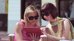 Female friends sitting outside while chatting and looking at tablet Stock Footage
