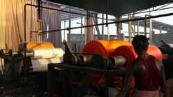 A workman walks around a machine rolling and washing newly dyed fabrics in a garment factory. Stock Footage