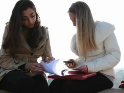 Teenage girls check text on marble rail, trees behind Stock Footage
