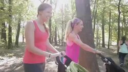 Young mothers exercising together in park, pushing toddlers in strollers Stock Footage