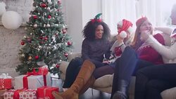 Friends laughing and hugging on sofa next to Christmas tree and gifts Stock Footage