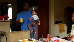 MS TS Father holding infant son while carrying glass of juice to daughter at breakfast table Stock Footage