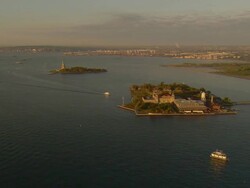 Aerial -Early morning wide shot of a ferry boat approaching Ellis Island with the Statue of Liberty behind. Stock Footage