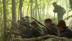 Union soldiers take cover in a forest and fire their rifles during a Civil War battle. Stock Footage