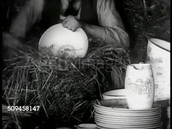 1936: MEMORABILIA: Two men in warehouse packing Wedgwood china. USA: Upscale couple in small shop, shopkeeper w/ Wedgwood plate. MS Wedgwood Edward VIII coffee service. CU Edward VIII mug. China & crystal displayed w/ prices cards. British Royalty. Instructional Video