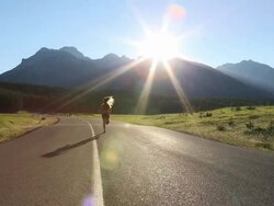 Teen girl runs down mountain road towards sunrise Stock Footage