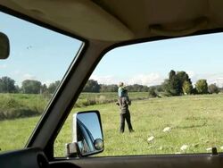 Father carrying young son on shoulders in a field, viewed from inside a car Stock Footage