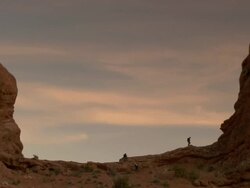 Hikers silhouetted along red rock ridge in desert - wide Stock Footage