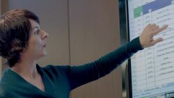 Insightful businesswoman leads meeting in corporate boardroom, points at spreadsheet data on big-screen Stock Footage