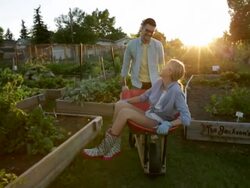 Man pushing woman in wheelbarrow though community garden Stock Footage