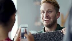 Girl takes smartphone photo of boy posing with sweater in trendy clothing shop Stock Footage