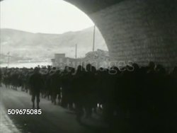 1942: U.S. & BRITISH FORCES: HA XWS US Soldiers on pier mobilizing, cargo ship BG. WS Silhouette of soldiers walking under viaduct. WS British soldiers walking. MS US Troops walking through North African town. MS Manning anti-aircraft gun. WWII Instructional Video