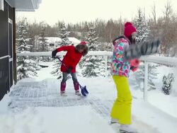 Mother and daughter shoveling snow off house deck Stock Footage