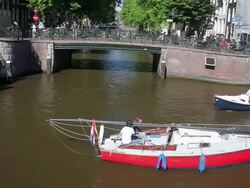 WS View of boats moving through canal while cyclists riding over bridge in background / Amsterdam, The Netherlands, Holland Stock Footage