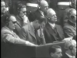 Lights in a courtroom dim and an audience watches footage of Hitler and other Nazi officials before a verdict is read. News Clip