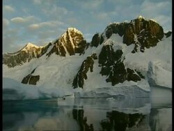 Tracking shot past icy mountains rising out of water, sun on peak, Antarctica Stock Footage
