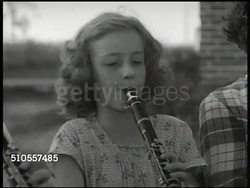 1950: SCHOOL BAND: Elder male teacher outside w/ children directing band, children w/ drums, girls playing clarinet, girls & boy playing drums, boys playing trumpets, teacher instructing trumpet section. Instructional Video