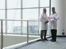 WS Physician standing in hospital lobby and second physician approaches to discuss a patient / Seattle, Washington, USA Stock Footage