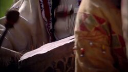 Male Native American Indian playing drum with two sticks next to standing female Stock Footage