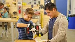 Hispanic preteen boy working with power tool at community woodworking day camp Stock Footage