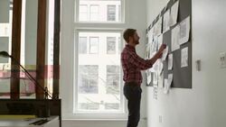 MS PAN Businessman pinning project ideas on board in office standing back and looking over work Stock Footage