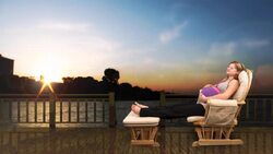 A pregnant woman relaxes in a glider against a computer generated lake at sunset. Stock Footage