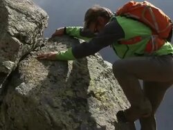 Man climbs rock ridge above mtns, looks out at summit Stock Footage