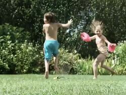 Boy and girl jumping through water from garden sprinkler Stock Footage