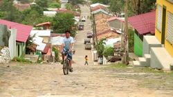 Boy pedals bike up cobblestone street in third-world country (slow-motion) Stock Footage