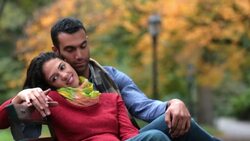 New York couple recline on park-bench in Central Park, holding hands playfully Stock Footage